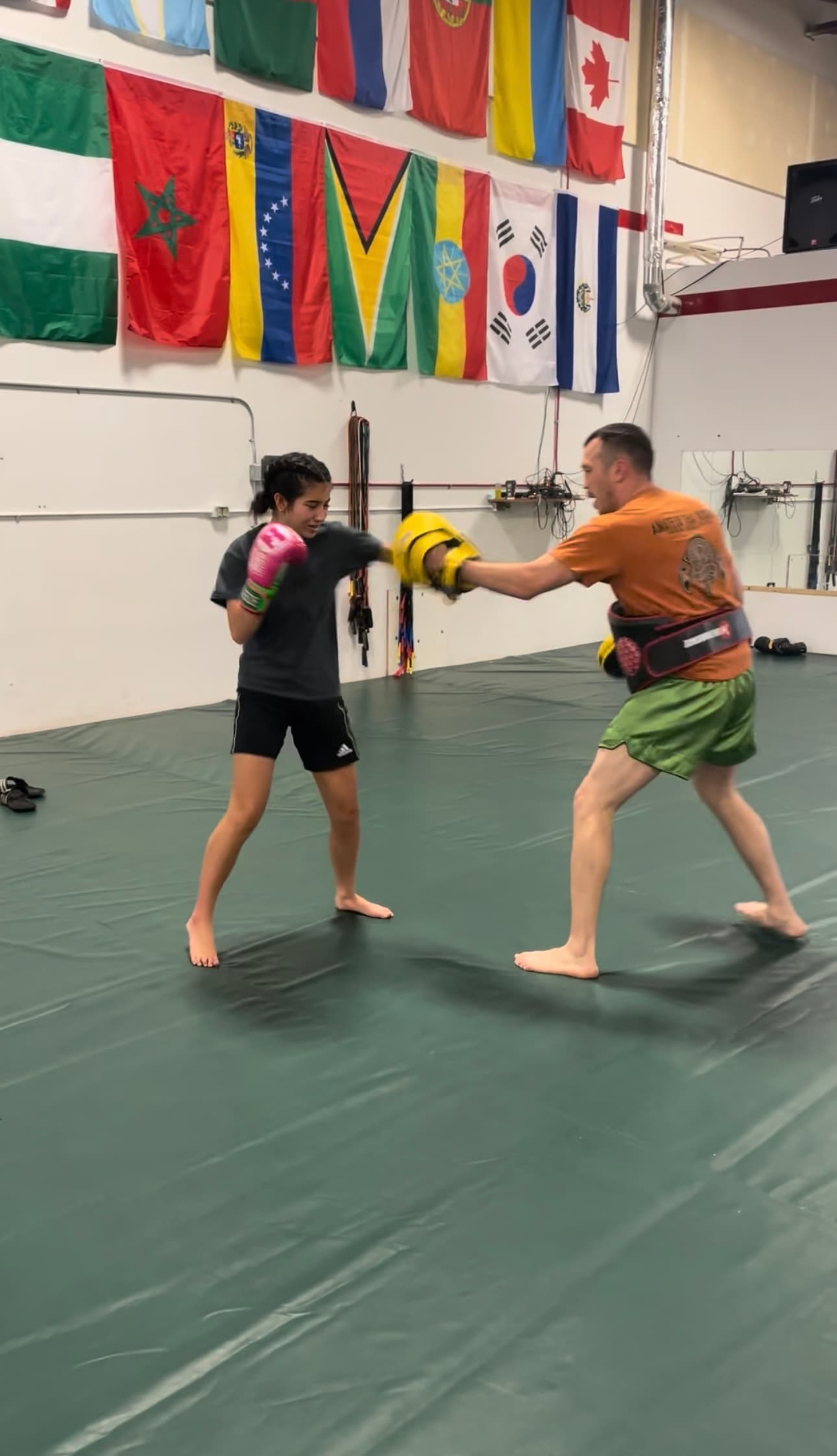 A young person punching focus mitts held by a coach in a boxing gym