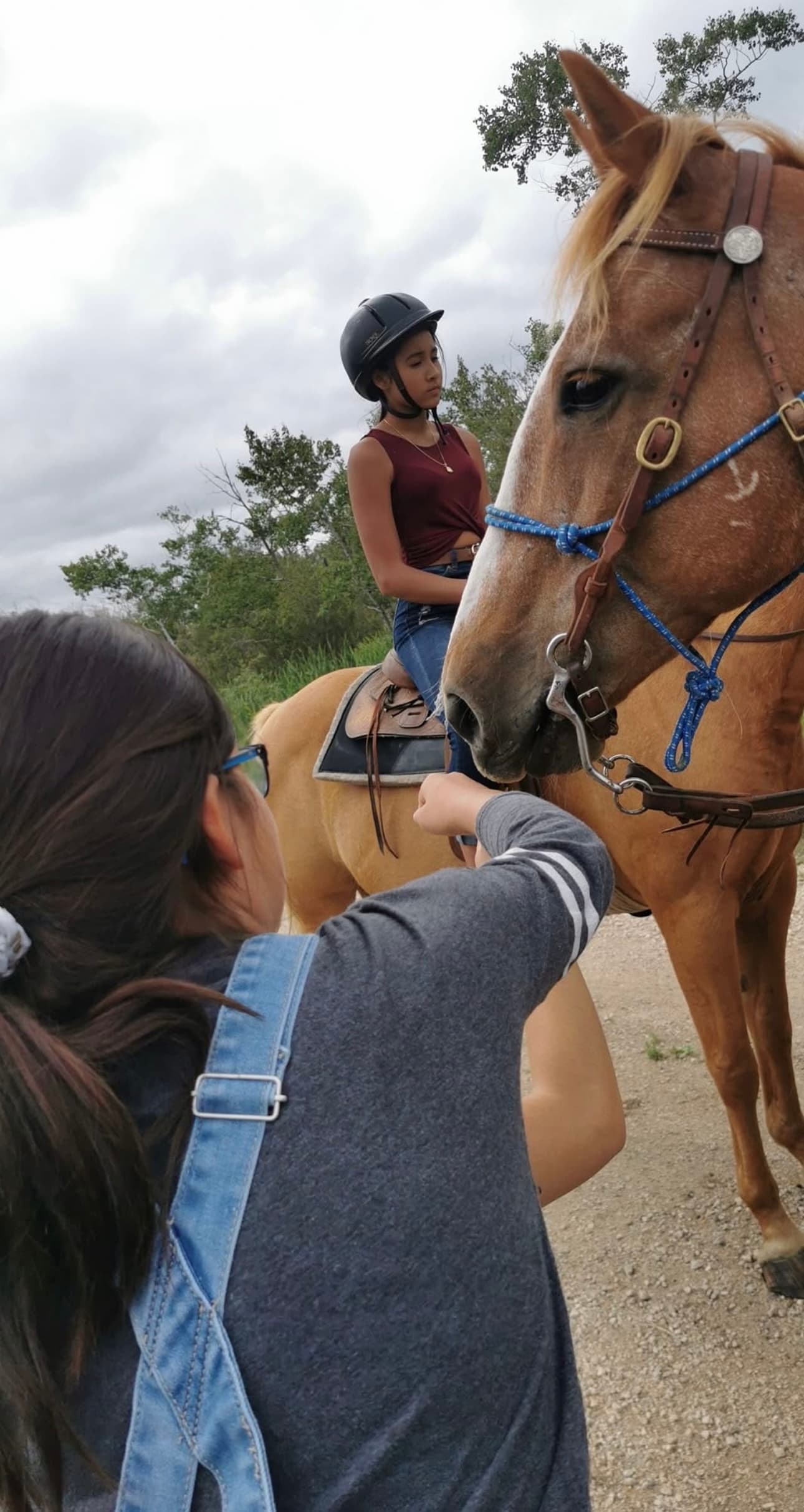 A young person riding a horse on a trail while another person steadies the bridle