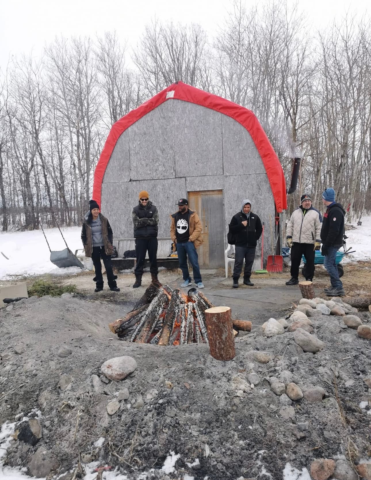 People standing around an outdoor fire in winter beside a canvas-covered shelter